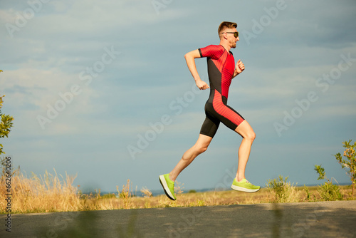 Speed and endurance. Motivated sportsman in sportswear running along the road, training outdoors. Side view. Concept of professional sport, triathlon preparation, competition, athleticism