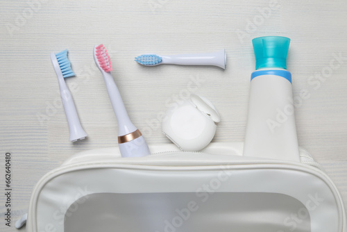 Electric toothbrushes, dental floss and tube in cosmetic bag on white wooden background, top view