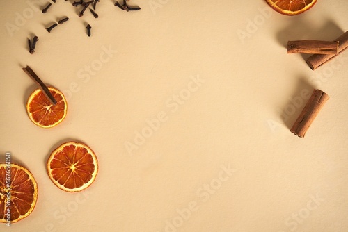 Arrangement of fresh oranges  cinnamon sticks  cloves  and Malcolm s seeds on a beige background.
