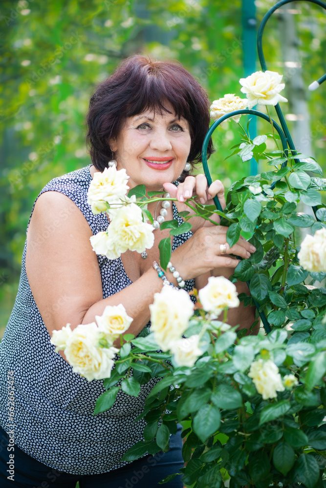 66-year-old woman in the garden. A mature woman enjoys the flowers of a rose grown with her own hands in her garden 66-year-old woman in the garden. A mature woman enjoys the flowers of a rose grown with her own hands in her garden