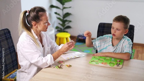 ABA Therapist Leads Therapy Session with Autistic Boy Using Color Cards; Rewards with Tokens; Bright Room with White Walls, Wooden Floor; Fiddle Leaf Fig (Ficus Lyrata) & Toys in the Background