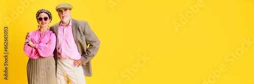 Beautiful senior woman in elegant clothes, beret and sunglasses standing with handsome man in smart casual outfit on yellow background. Concept of beauty and fashion, relationship, modern style, age