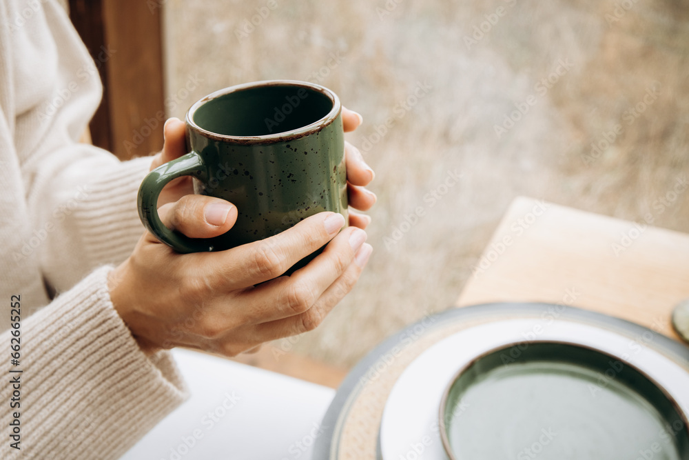 Women's hands in a warm light-colored sweater holding a cup of hot drink . Morning coffee, autumn breakfast