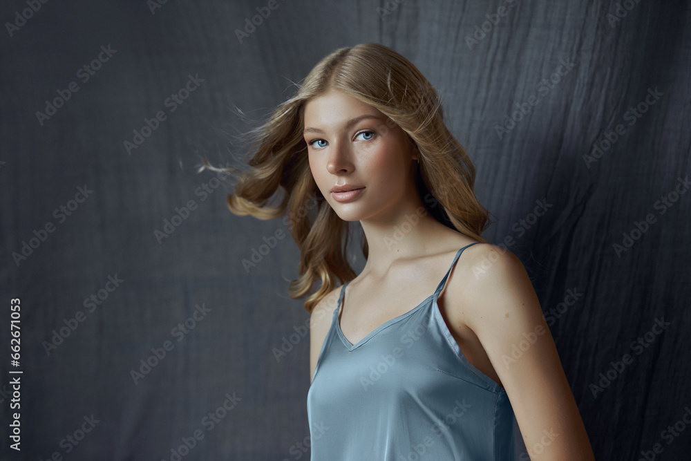 Portrait of a young woman in a light gray silk dress. Beautiful makeup, blue eyes of a blonde woman. Curly hair Portrait of a young woman in a light gray silk dress. Beautiful makeup, blue eyes of a blonde woman. Curly hair