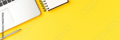 Elegant office desktop with laptop, notebook and pen on yellow background with copyspace. Modern workspace photo