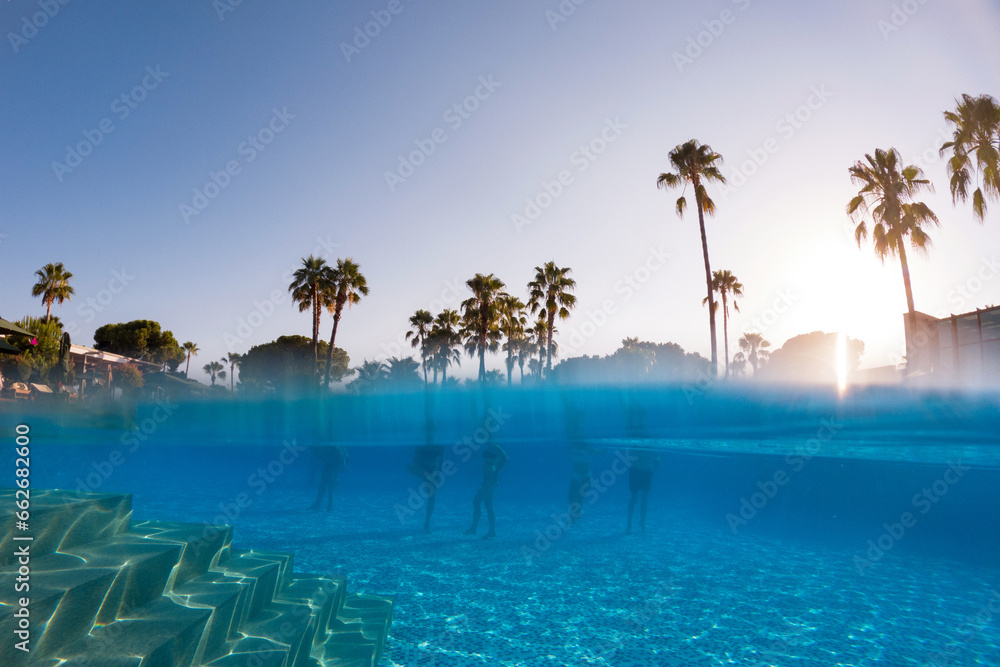 Underwater photography of people standing in pool with copy space. Beach resort vacation by sea. Winter or summer seaside resort holiday. Over-under underwater photography.