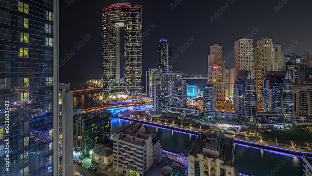 Panorama showing Dubai Marina with several boat and yachts parked in harbor and skyscrapers around canal aerial night timelapse.