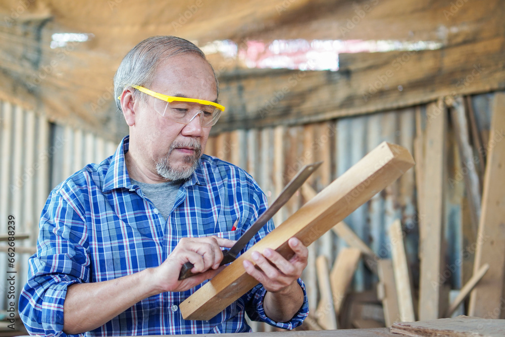 Asian senior male carpenter equals a wooden bar in the workshop with wood boards background. copy space Asian senior male carpenter equals a wooden bar in the workshop with wood boards background. copy space