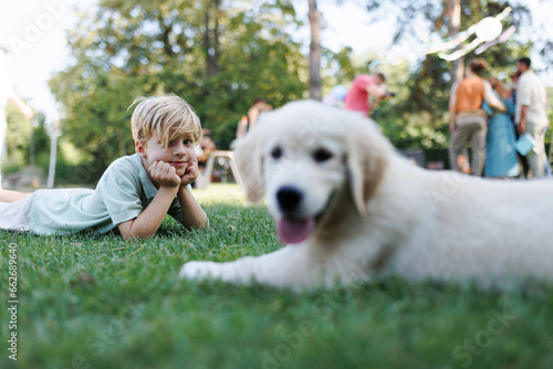 Children playing with a small puppy at a family garden party. Portrait of little boy lying on grass with Golden retriever puppy.