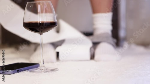 A woman is sitting on the toilet in the bathroom. A woman is sitting in the toilet with a glass of wine and a phone.