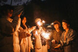 Group of multiethnic friends holding sparklers with happy expression. Young men and women enjoying out with fireworks.