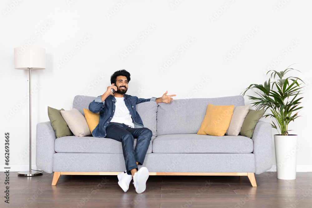 Positive young indian guy chilling on couch, have phone call Positive young indian guy chilling on couch, have phone call