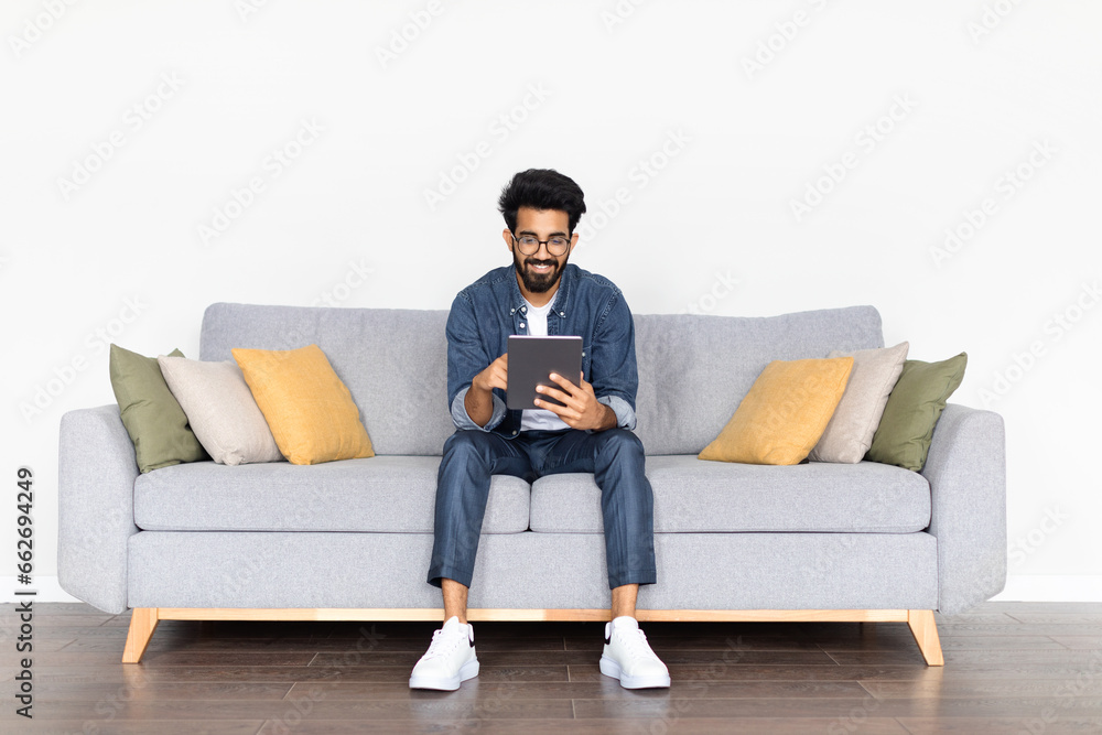 Relaxed Indian Guy Browsing Digital Tablet While Sitting