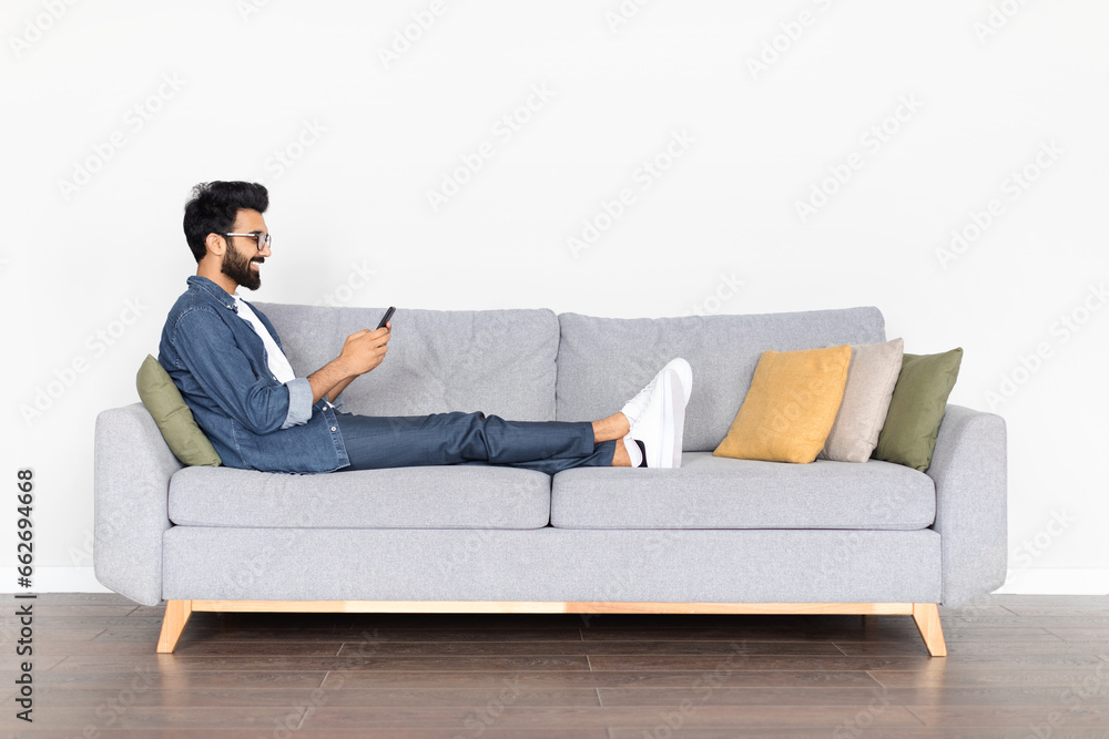 Young Indian Man Engaging with Smartphone on Sofa Young Indian Man Engaging with Smartphone on Sofa