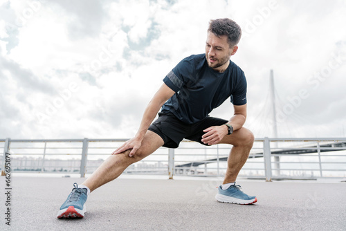 Runner man smiles exercise stretching leg muscles active lifestyle. Mental health and motivation for training. Warm-up fitness workout in sportswear interval training.
