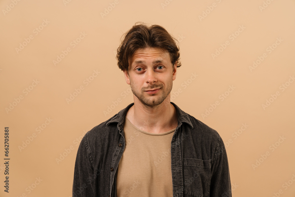 Young man smiling at camera while standing isolated over beige wall Young man smiling at camera while standing isolated over beige wall