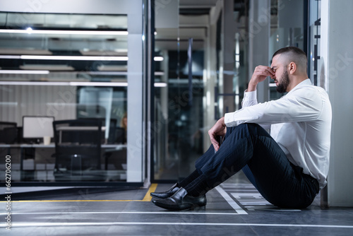 Sad bankrupt businessman sitting on the floor in office. Disappointment and loss in business and career.