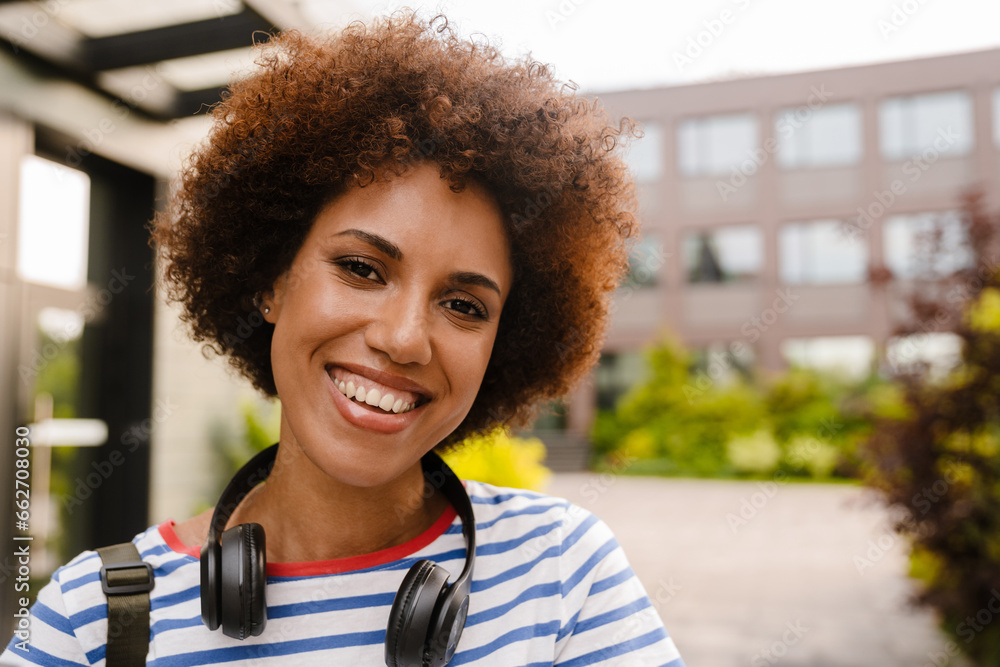 Fototapeta premium Portrait of happy female student smiling at camera while standing in campus