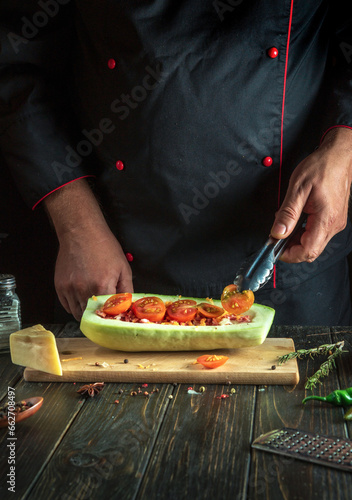 Fototapeta Naklejka Na Ścianę i Meble -  Experienced chef adds a tomato to the zucchini. The concept of cooking a national stuffed squash boat or marrow in a restaurant kitchen.