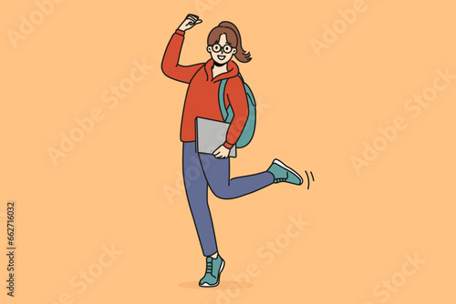 Cheerful student girl makes victory gesture and holds books in hands, rejoicing at receiving quality education. Young woman student with backpack smiling celebrating entering college or university