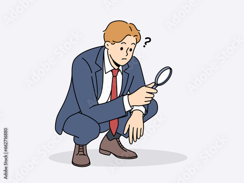 Business man with magnifying glass squats doing work of analyst or supervisor conducting audit. Guy in business suit is independently investigating causes of financial problems in company