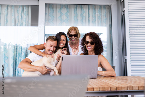 Traditional family with their dog are on the terrace of their house while making a video call all together through the laptop.
