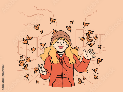 Little girl throws up leaves of autumn trees walking in park and rejoices at end of summer and onset of september. Happy child in autumn jacket and hat laughs standing among falling maple foliage