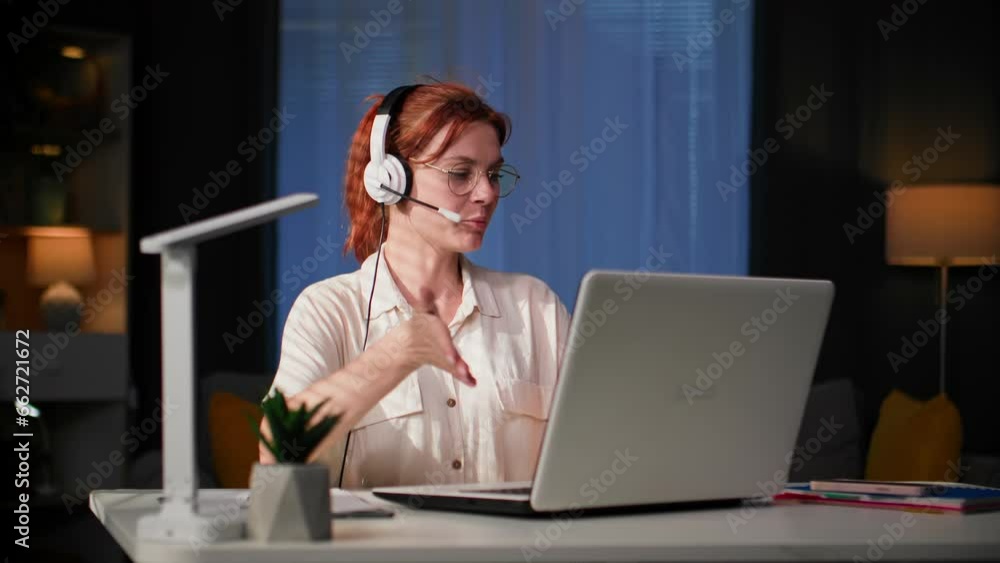 home office, young woman in glasses communicates online using a headset and video communication on a laptop with her boss and makes notes in a notebook while sitting at her desk at home home office, young woman in glasses communicates online using a headset and video communication on a laptop with her boss and makes notes in a notebook while sitting at her desk at home