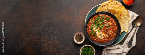 Traditional Indian Punjabi dish Dal makhani with lentils and beans in black bowl served with naan flat bread, fresh cilantro and two spoons on brown concrete rustic table top view. Space for text. photo