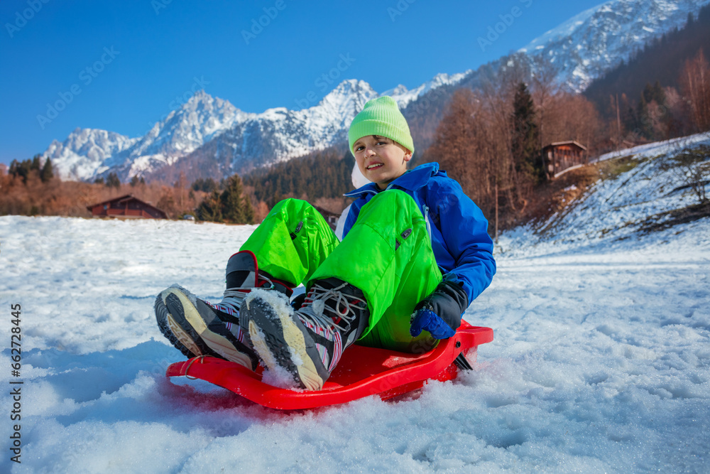 Young boy in winter outfit slide downhill on alpine slope