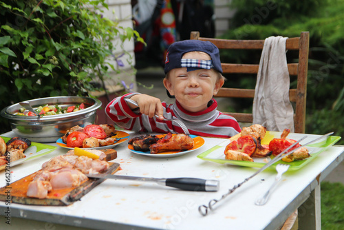 a child with a contented face is sitting at a table full of food. A child has a good apetite. photo