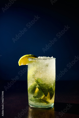 freshening glass of mojito garnished with mint and lime slices on dark background, concept