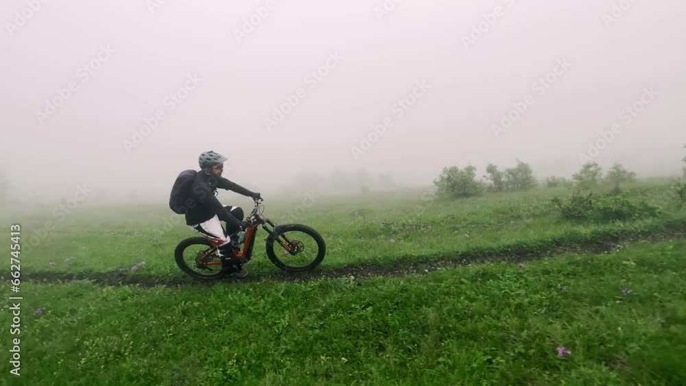 Man extreme bicycle riding on thin path mountain green grass with fog mist aerial view. Male enduro electric bike cycle driving on dirt off road way with natural greenery vegetation hilly terrain 4k Man extreme bicycle riding on thin path mountain green grass with fog mist aerial view. Male enduro electric bike cycle driving on dirt off road way with natural greenery vegetation hilly terrain 4k