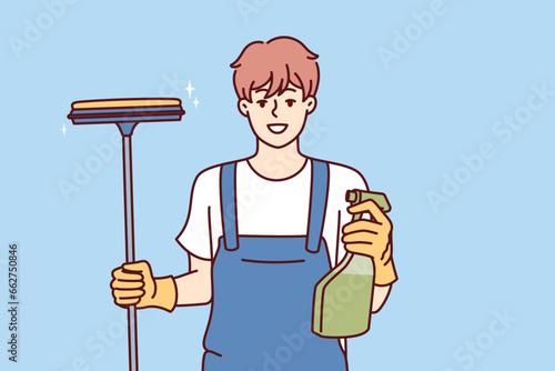 Happy man window cleaner holds spray bottle with detergent and mop for cleaning glass and glossy surfaces. Professional janitor provides window cleaning services in business centers and offices