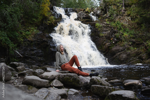 a young beautiful woman tourist sitting against the backdrop of a waterfall surrounded by forest