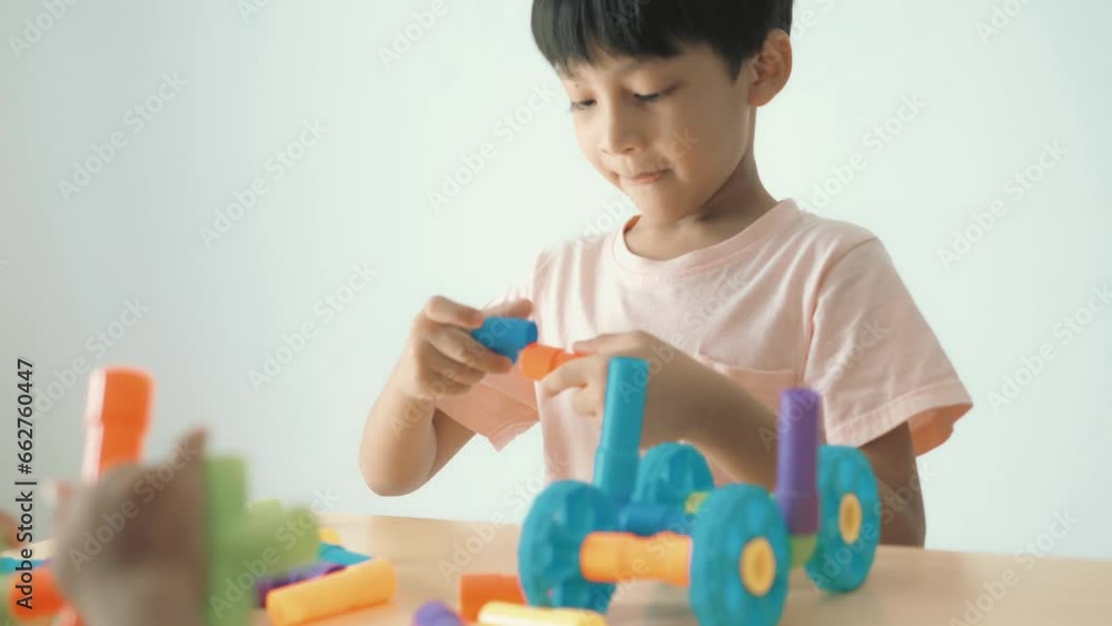 Adorable Asian boy, about 3-6 years old, wearing a pink shirt, happily playing with a puzzle shaped like a water pipe and having various toy items placed on a table inside his home, white background. Adorable Asian boy, about 3-6 years old, wearing a pink shirt, happily playing with a puzzle shaped like a water pipe and having various toy items placed on a table inside his home, white background.