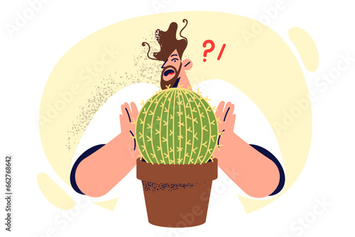 Stupid man touches cactus in flower pot with hands and gets fingers cut due to carelessness