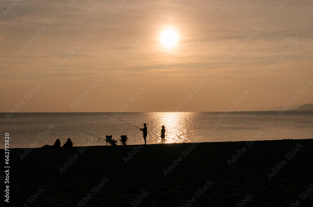 Couple catching fish at sunset, silhouette, coast, calm.