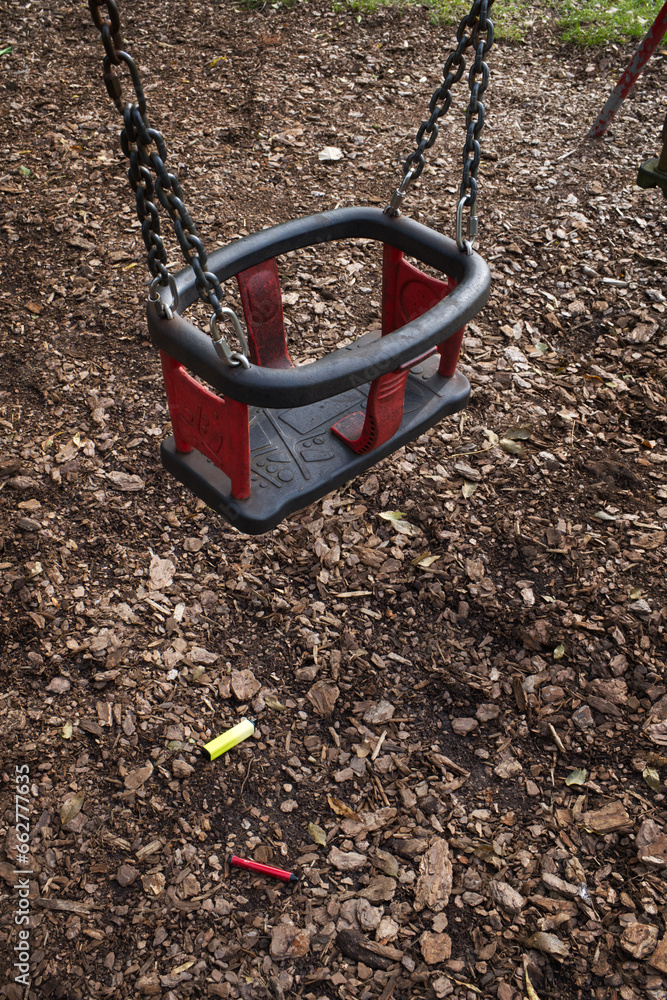 Two brightly coloured electronic cigarette vapes left underneath a child's swing in a play park