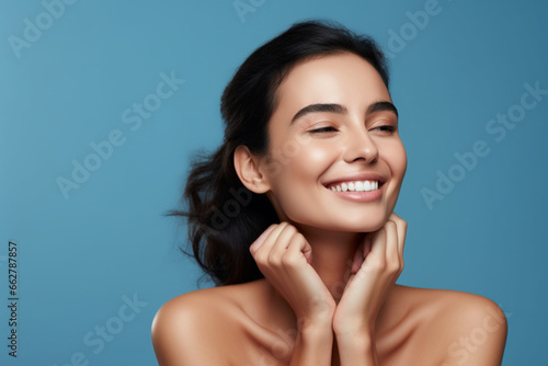 Beautiful woman hold folded palm near face, Millennial lady enjoying soft smooth skin on hand face, Smiling model looking aside, Studio portrait on blue