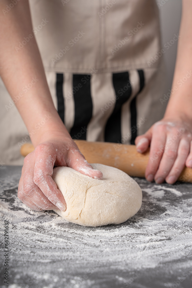 The process of preparing pizza dough. Female hands preparing dough on a dark background. Ingredients for the dough.