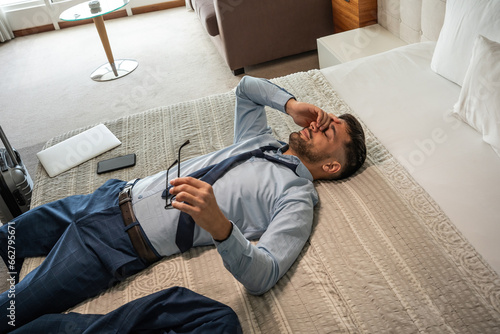 The businessman enters his hotel room, with a sense of relief, sinks onto the hotel bed. The comfort of the room offers a well-deserved moment after a long day of meetings.