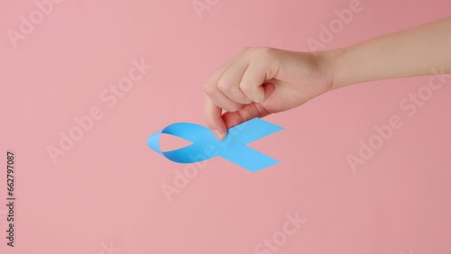 Vertical shot of female hand holding blue ribbon, posing over pink background with copy space for design. Healthcare, International men, Father and World Cancer Day concept. Symbol for support men photo