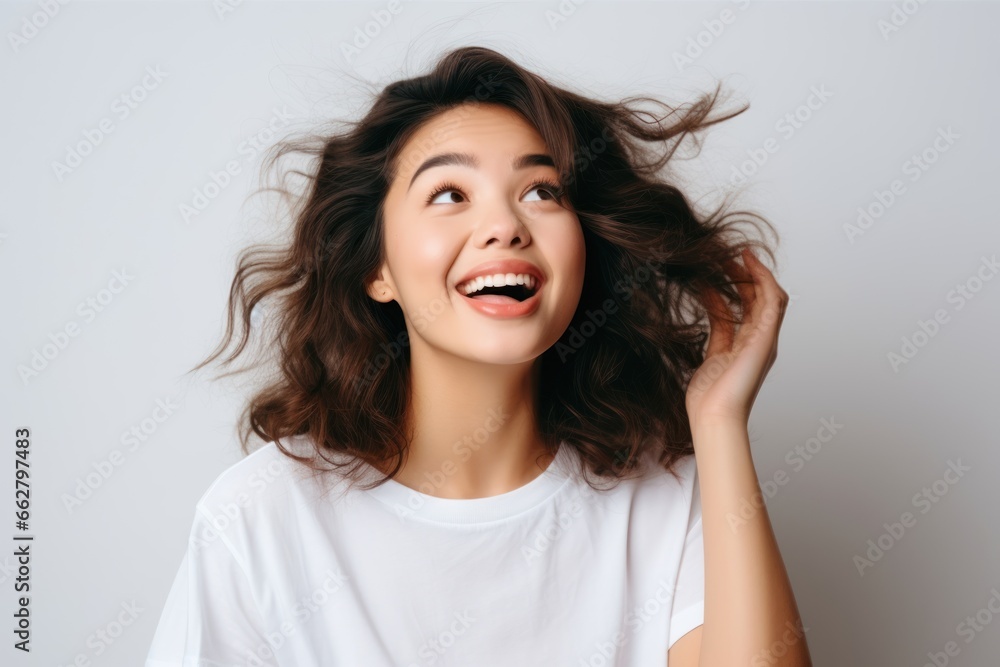 Beautiful young girl with curly hair in white t-shirt cheerfully smiling over grey background. Happiness. Human emotions Beautiful young girl with curly hair in white t-shirt cheerfully smiling over grey background. Happiness. Human emotions