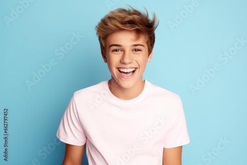 Handsome, smiling teen boy with stylish hairstyle, in casual white t-shirt against blue studio background. Human emotions photo