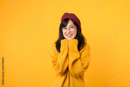 Expressing her shy side with a smile. A lovely lady, in a red beret and yellow sweater, radiates positivity against a vibrant yellow backdrop. © Jirawatfoto