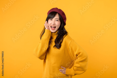 Young Asian woman in her 30s making a stylish announcement, wearing a yellow sweater and red beret against a vibrant yellow background. Expressive and dynamic communication. © Jirawatfoto