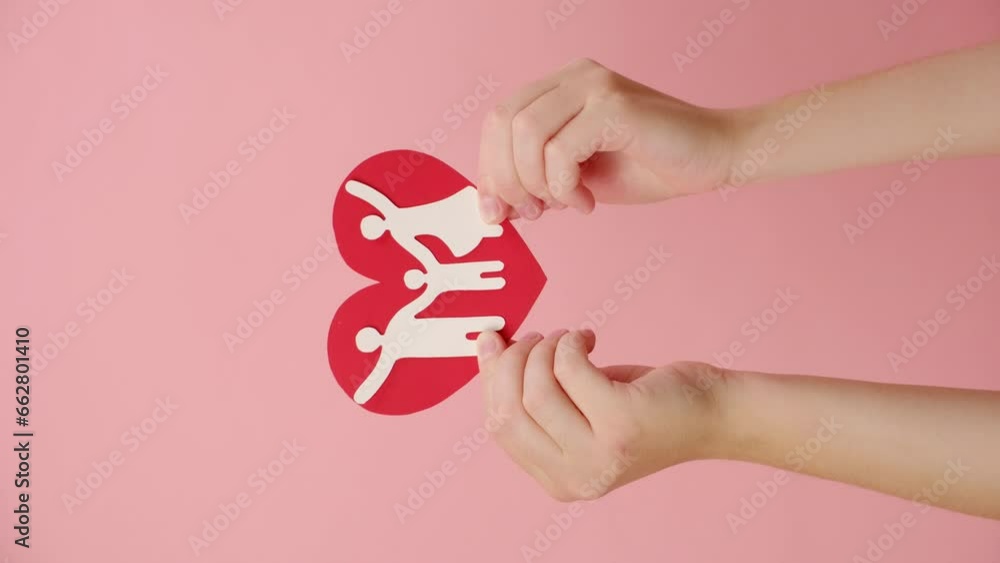 Vertical shot of female hand holding paper family cutout on heart, isolated over pink studio background, family, foster care, world mental health day, Autism support, budgeting cost of living concept Vertical shot of female hand holding paper family cutout on heart, isolated over pink studio background, family, foster care, world mental health day, Autism support, budgeting cost of living concept