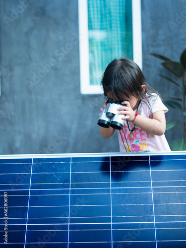 Happy Asian girl admiring solar panels with binoculars recently installed at home.