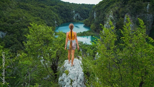 Athlete rock climber teen girl on mountain top looking on lake with turquoise water and high waterfalls. Tourist woman in Plitvice Croatia.
